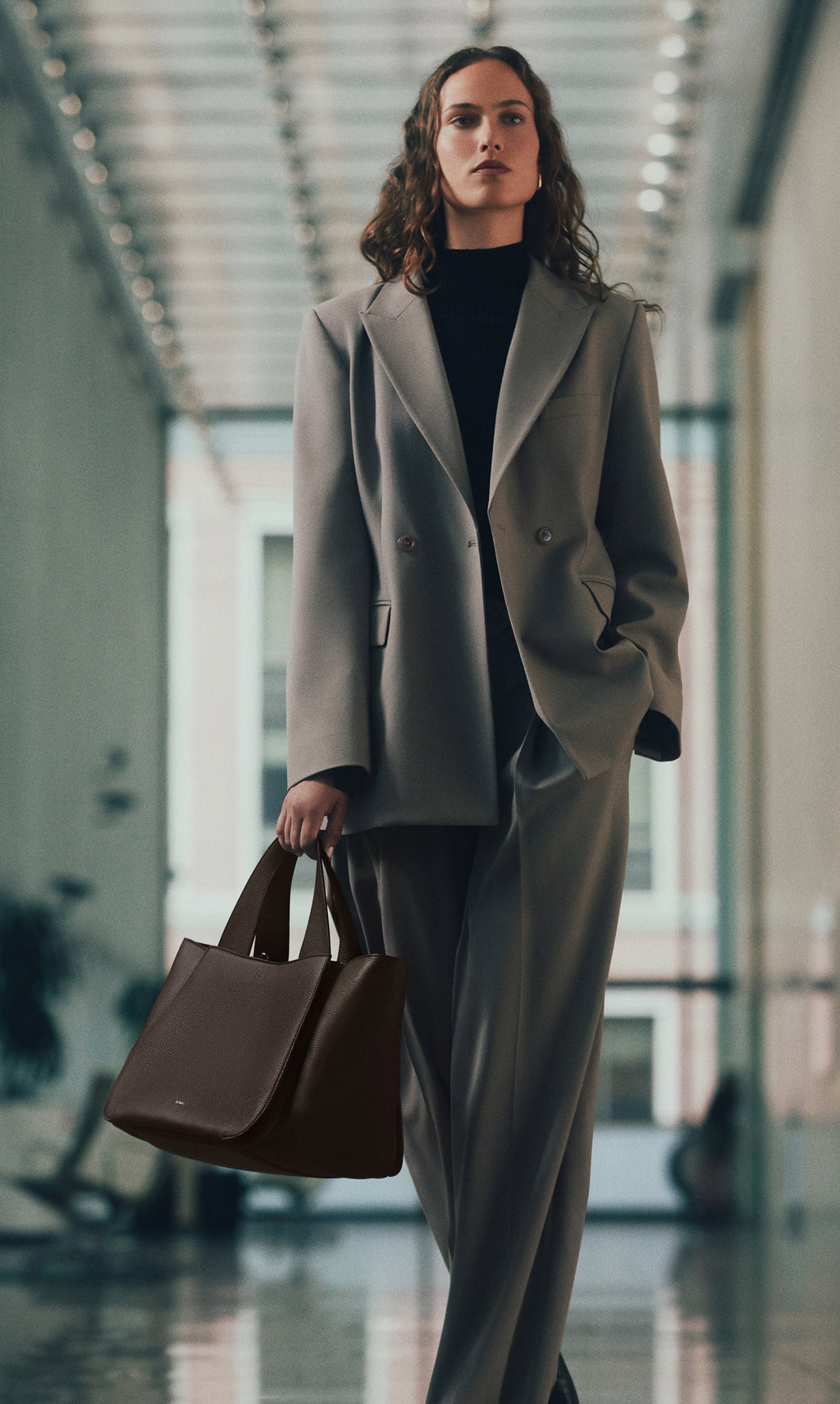 Person in a suit walking indoors holding a large handbag