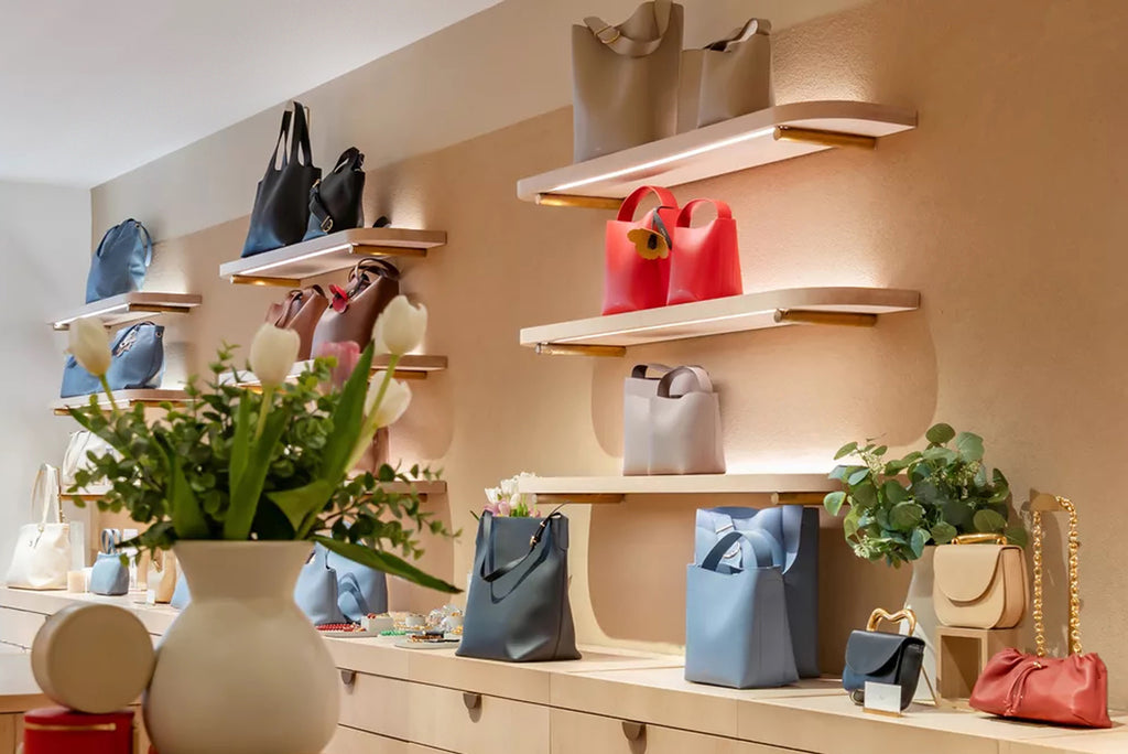 Handbags displayed on wall shelves above a counter with vase and plants in a store.