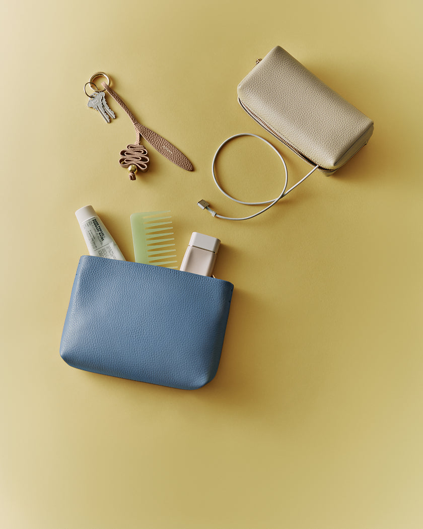 Two pouches, keys, comb, lotion, charger cable, and a lipstick on a solid background.