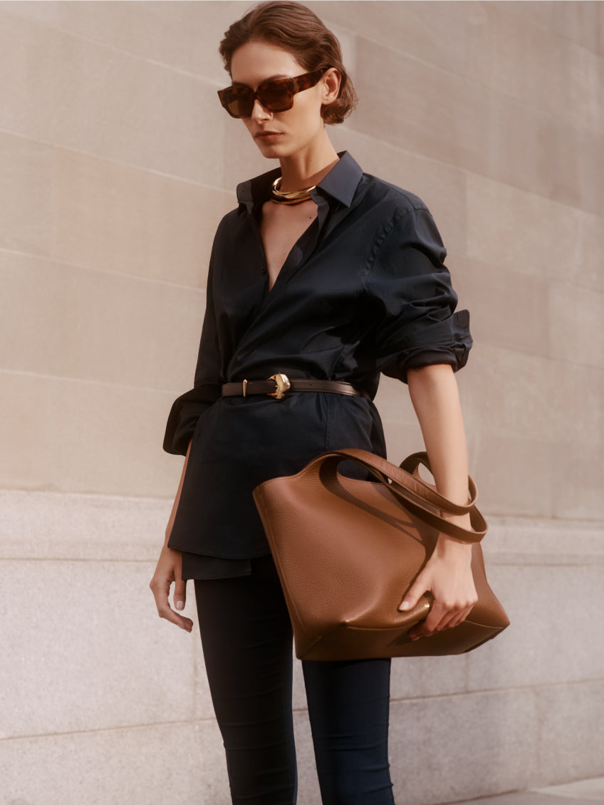 Person wearing sunglasses, carrying a large bag, dressed in a shirt and pants.