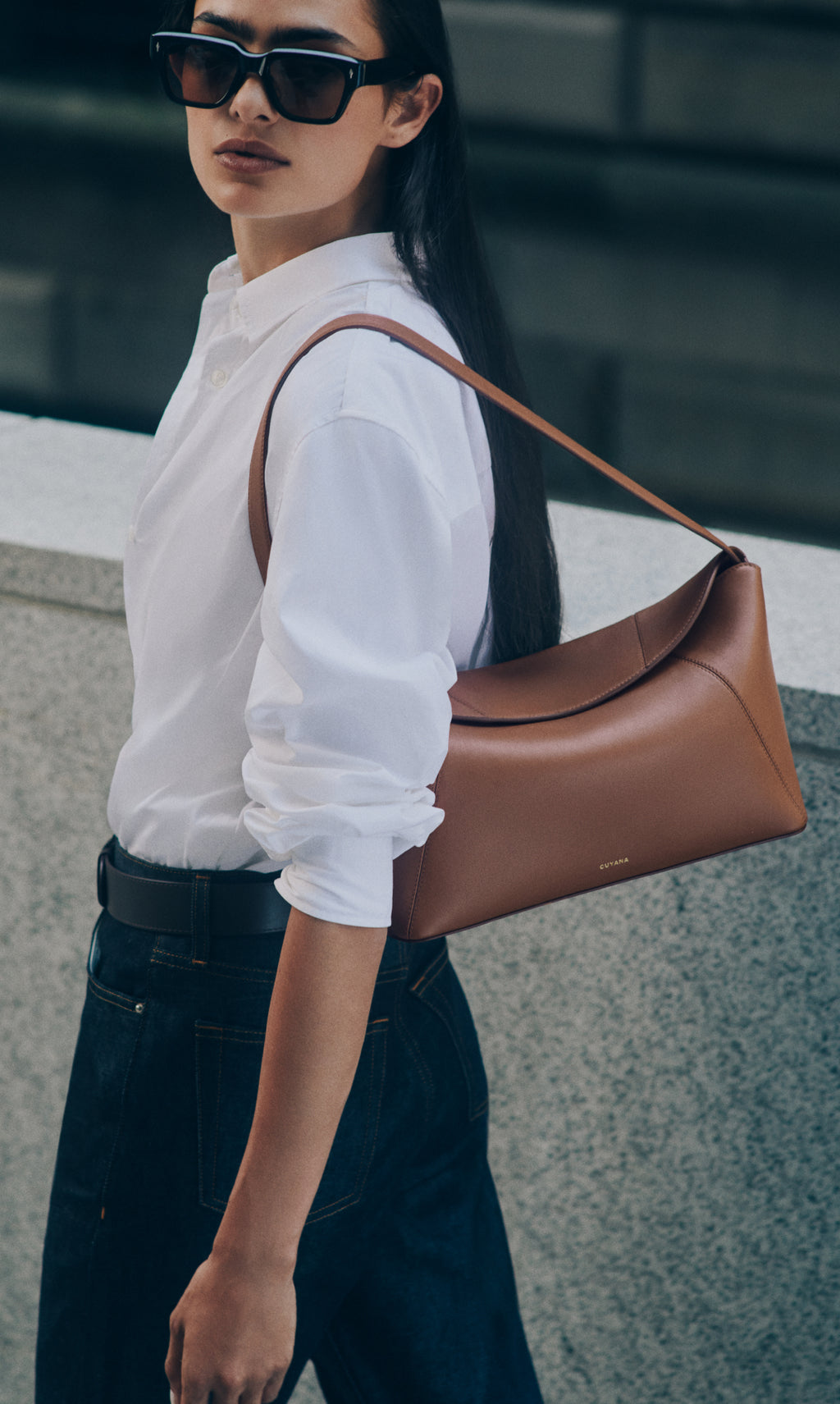 Person wearing sunglasses and carrying a shoulder bag over one shoulder.