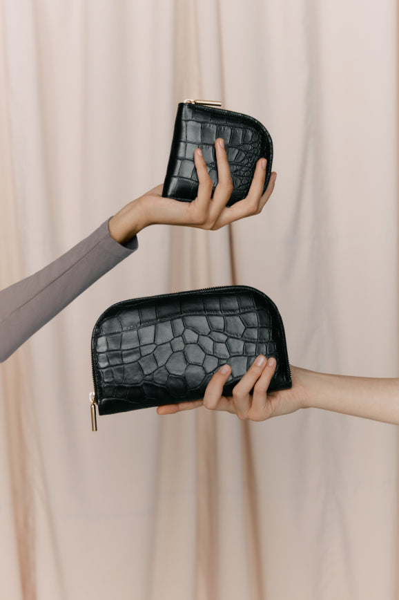Two hands holding small pouches against a draped background.