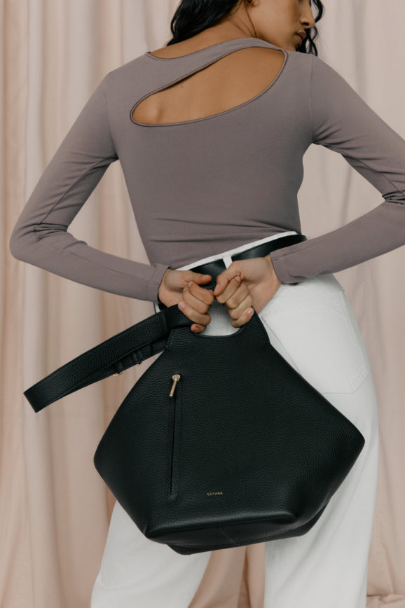 Woman holding a handbag, viewed from behind, shirt with cut-out back.