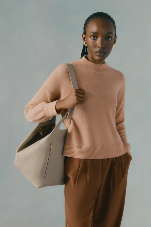 Woman holding a bag and wearing a sweater and trousers.