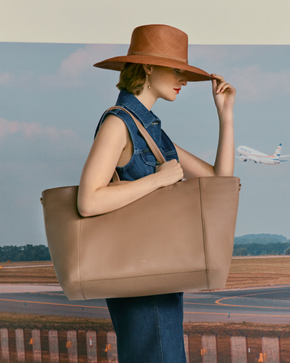 Woman holding large bag at an airport with a plane in the background.