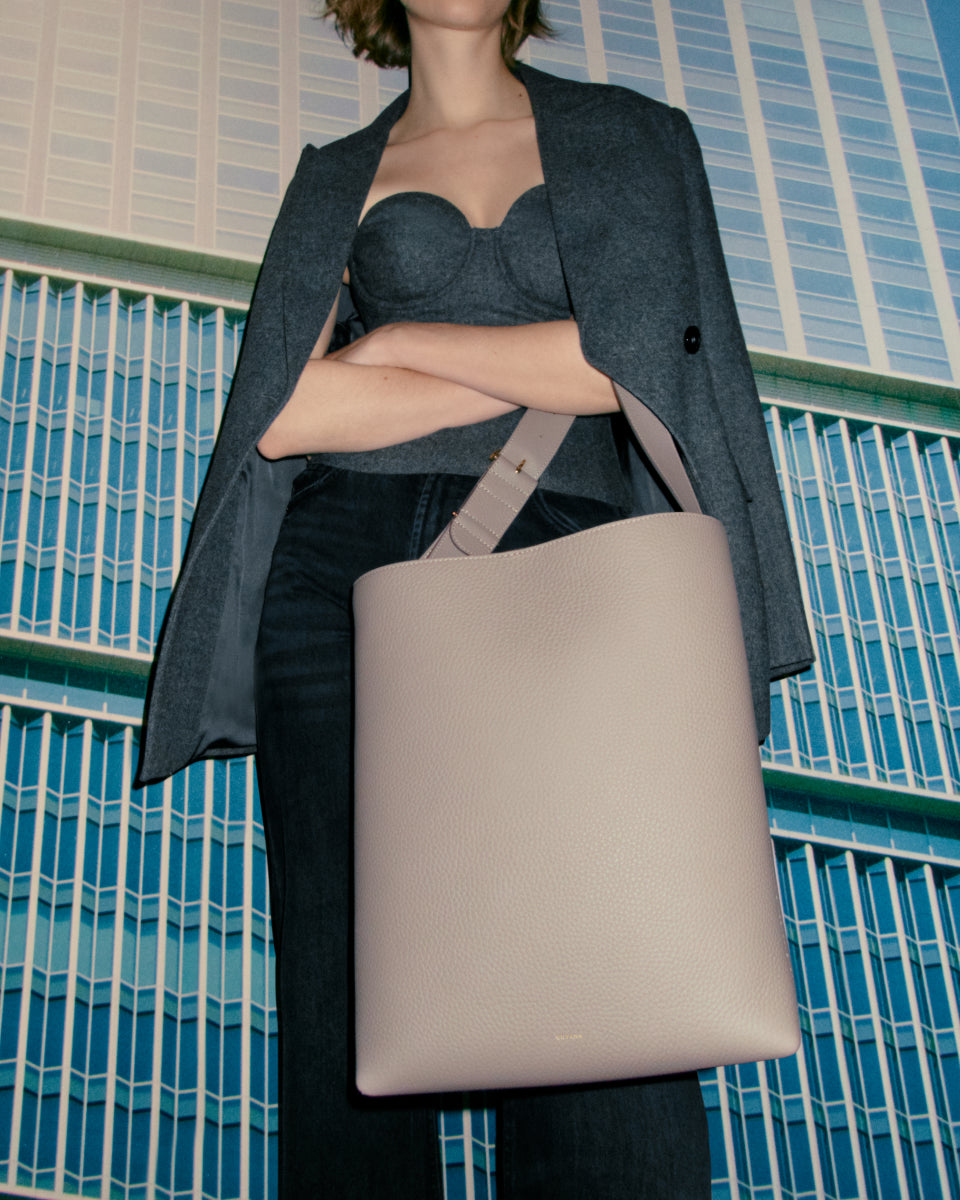Woman standing with a handbag in front of a tiled wall.