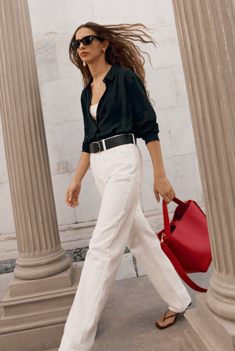 Woman walking by columns with sunglasses and a handbag.