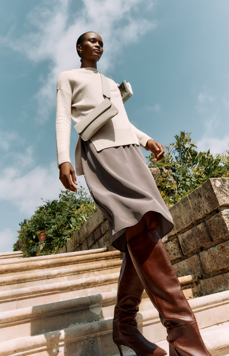 Woman standing on stairs wearing a long skirt, top, and boots.