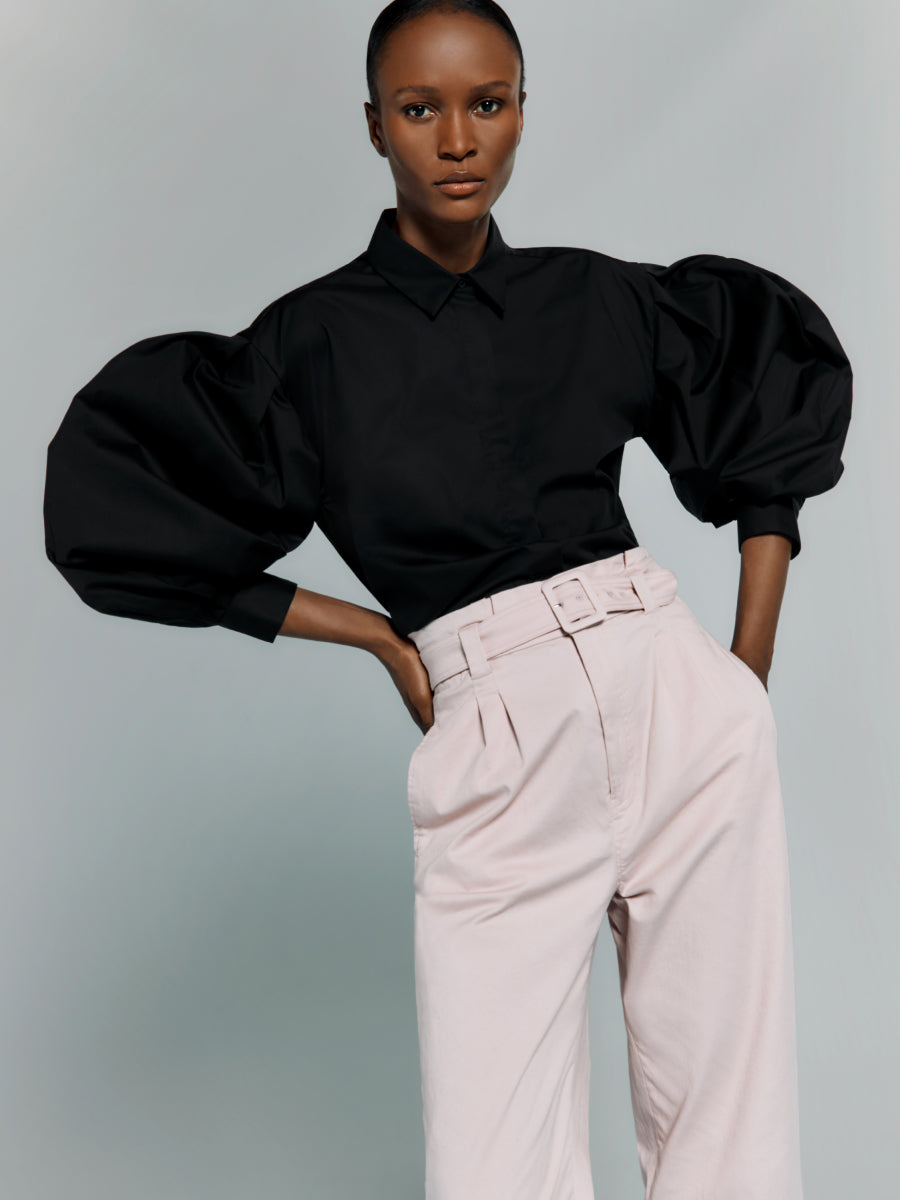 Woman standing with hands on hips in a puffy-sleeved top and pants.