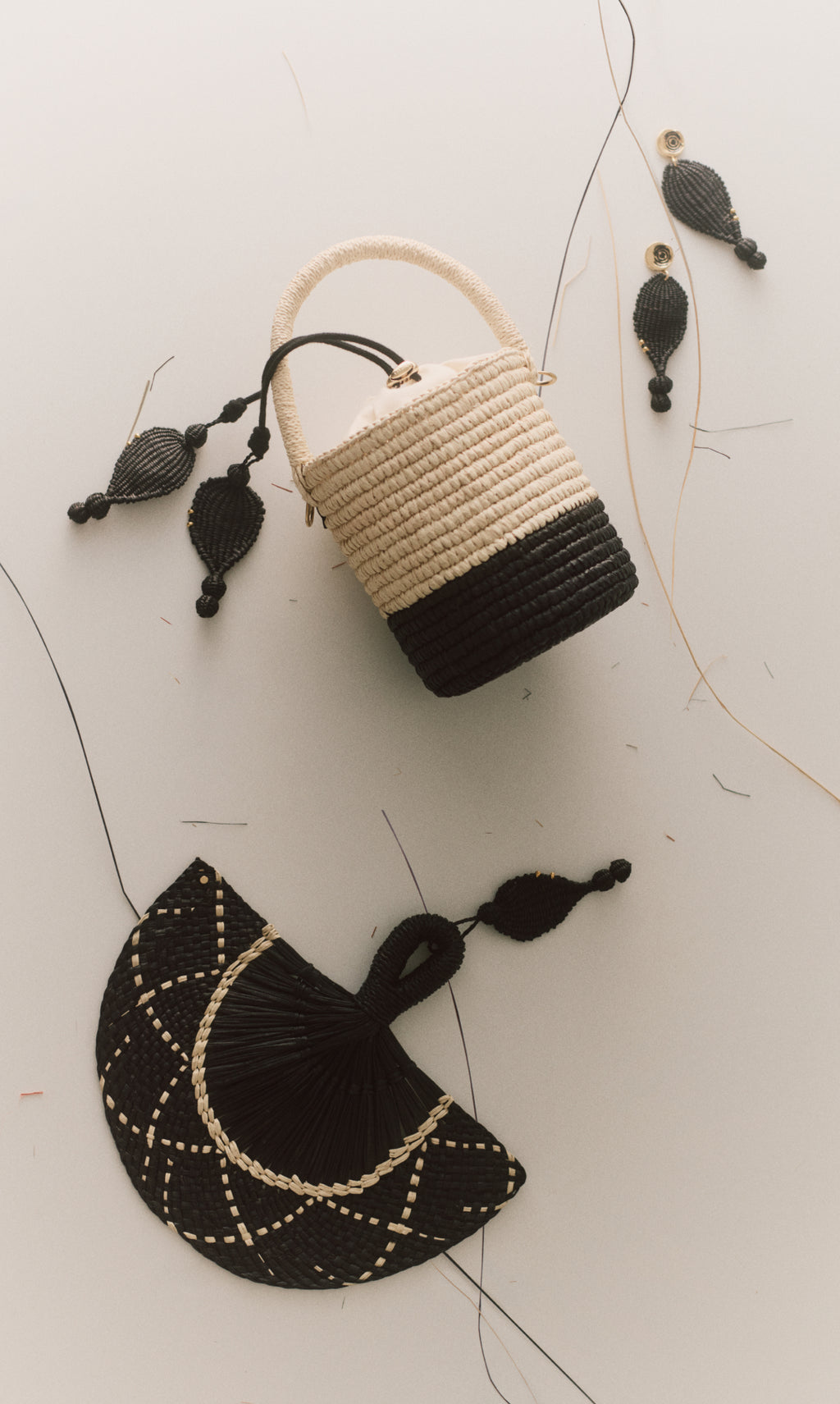 Woven basket bag with handle, earrings, and fan laid on surface.