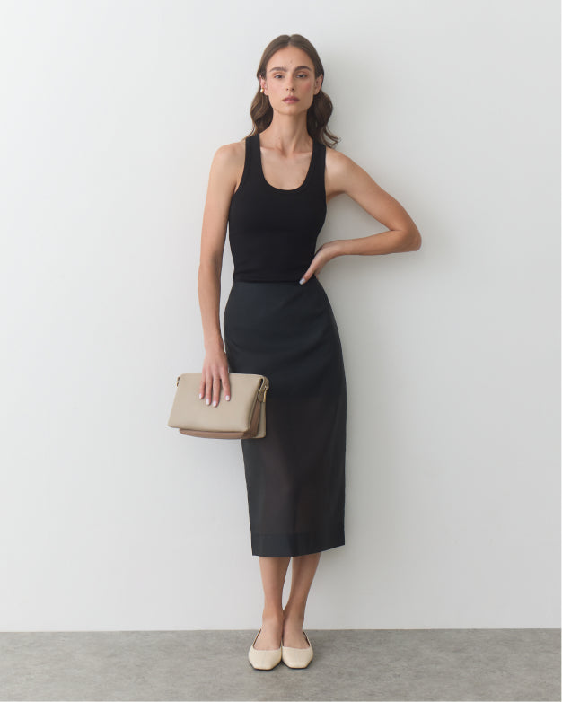 Person in a sleeveless top and long skirt holding a clutch bag.