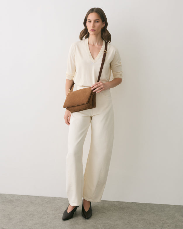 Person in outfit with a crossbody bag stands against plain backdrop.