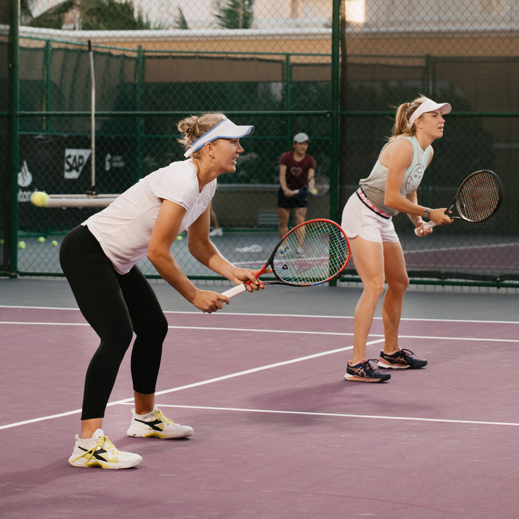 Two women playing doubles tennis on an outdoor court.