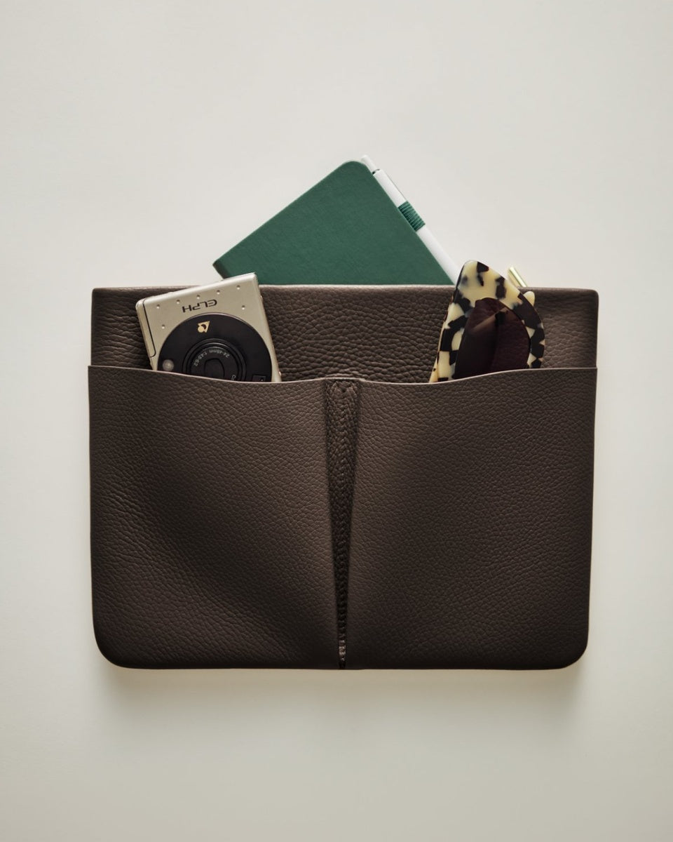 Leather pouch with camera, notebook, and scarf peeking out from pockets