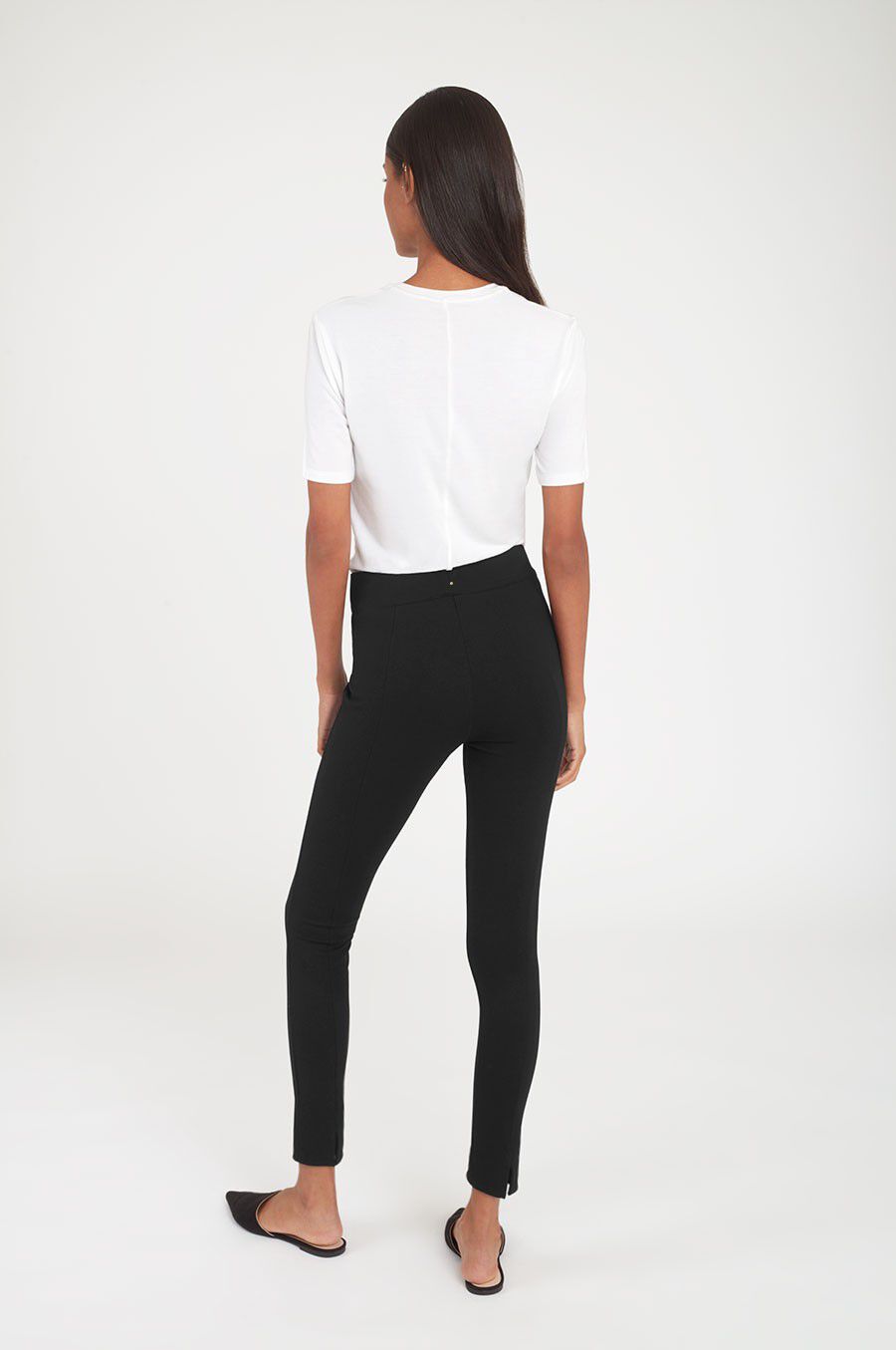 Woman standing, viewed from behind, wearing a top and slim-fit pants.
