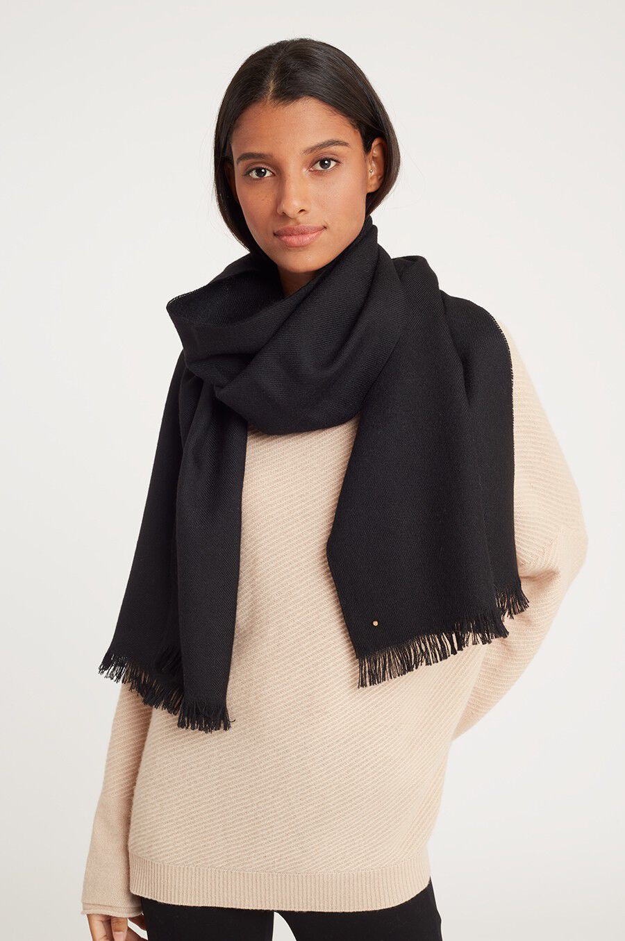 Woman wearing a sweater and large scarf, looking at camera.