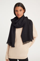 Woman wearing a sweater and large scarf, looking at camera.