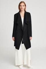 Woman standing in an open long coat over a top and wide pants with shoes.