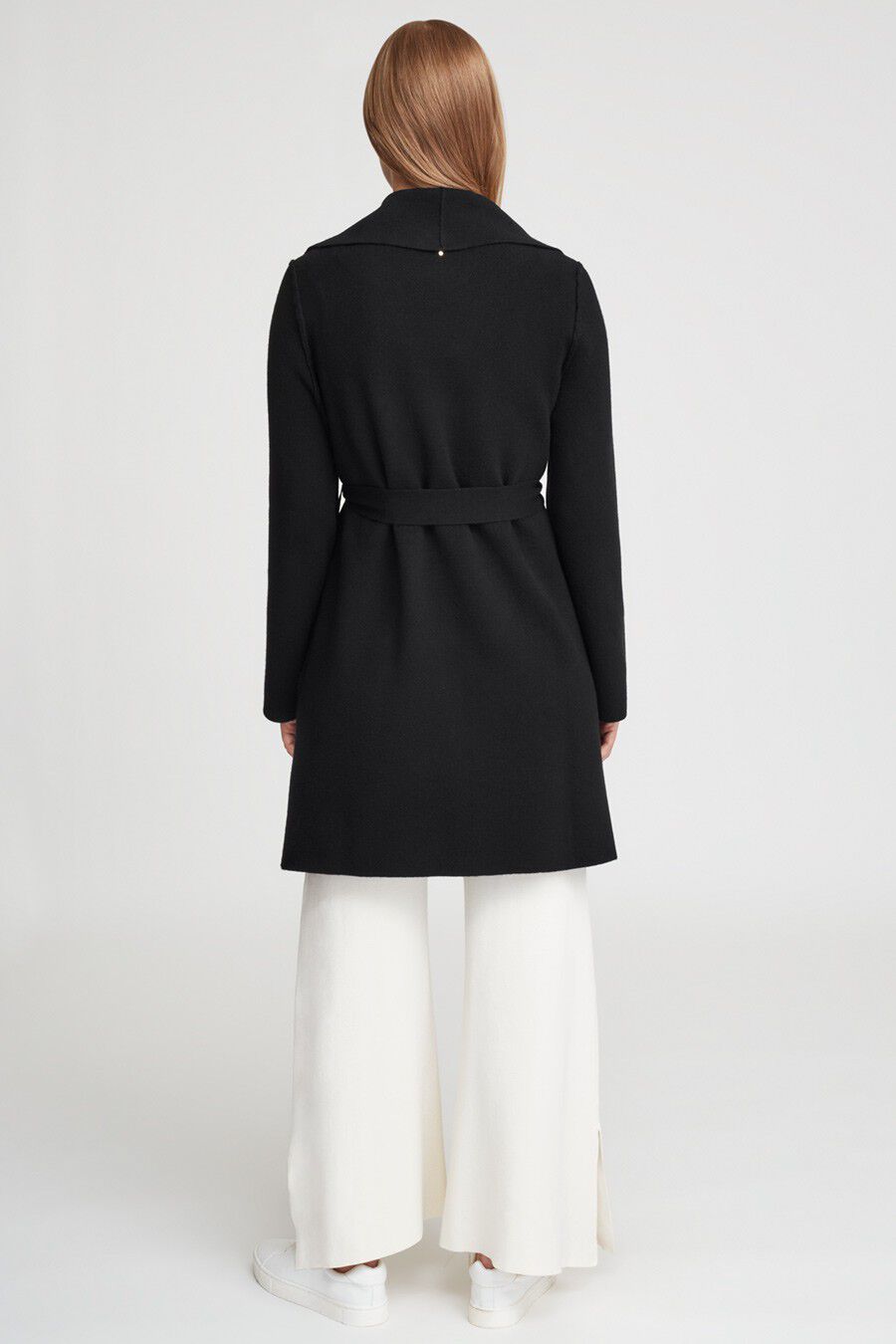 Person standing facing away wearing a long coat and wide-leg trousers.