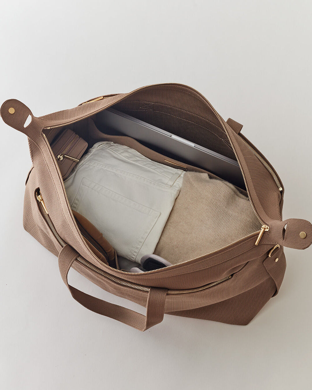 Open bag with a laptop and folded pants inside.