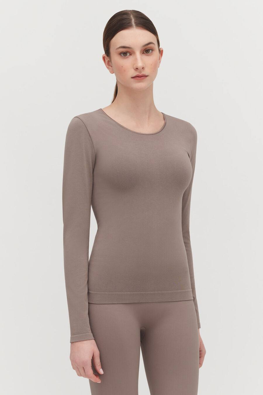 Woman standing in a long sleeve top and fitted pants, looking at the camera.