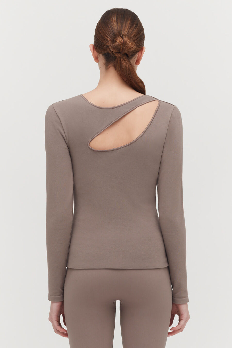 Woman facing away, wearing a top with a back cut-out and hair in a bun.