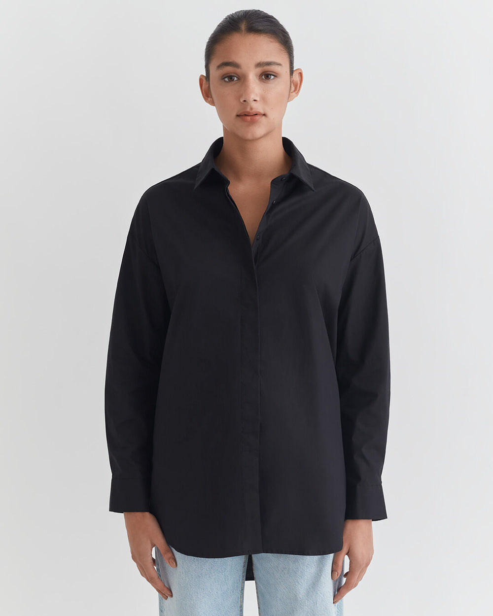 Woman in a button-up shirt and jeans standing against a white background.