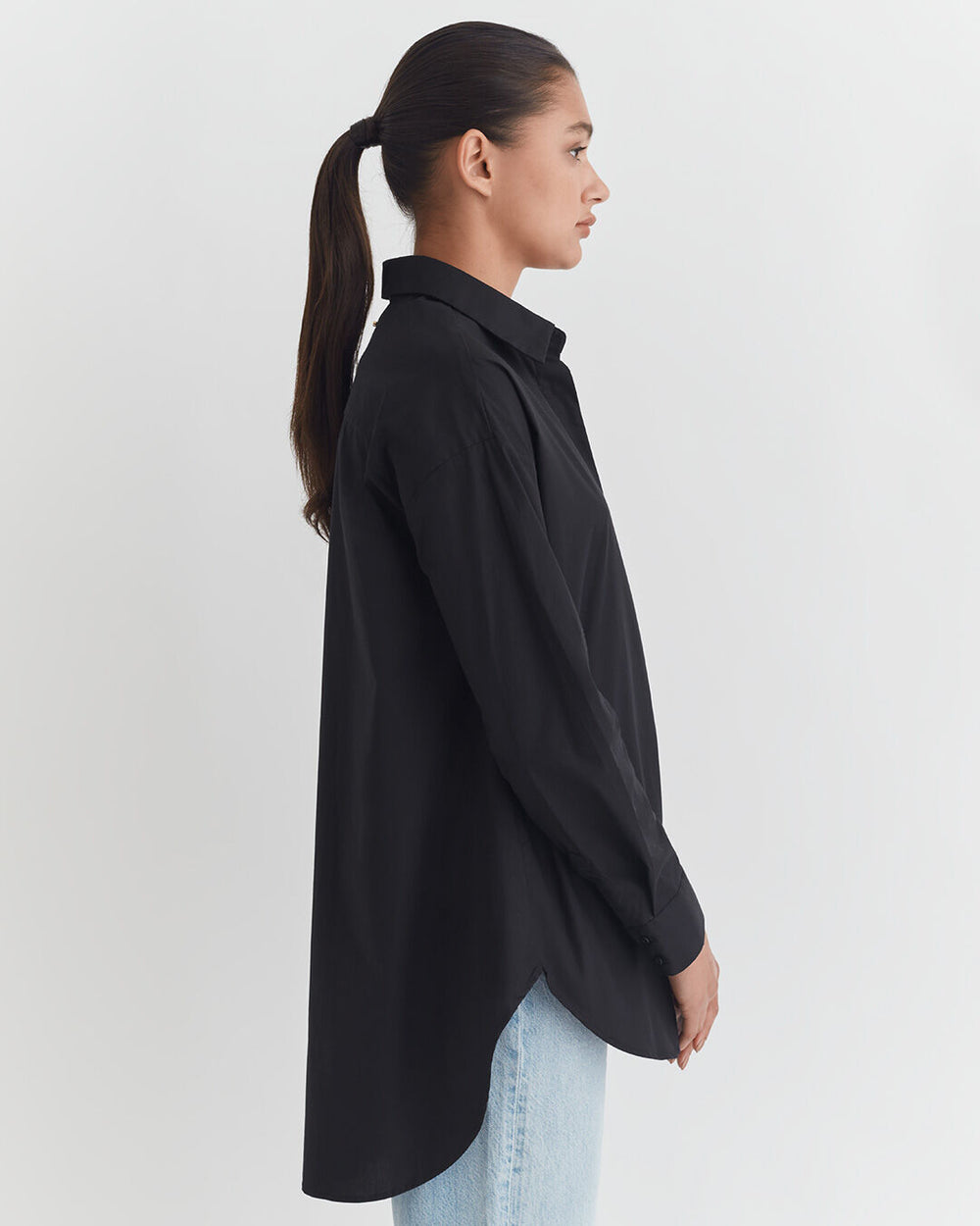 Woman in a buttoned shirt and jeans viewed from the side with hair in a ponytail.