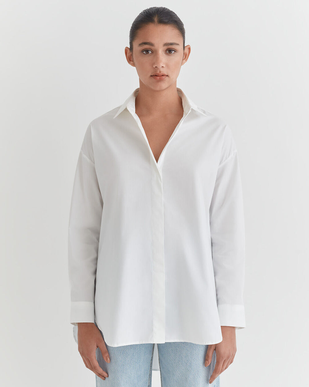 Woman in a button-down shirt and jeans standing against a plain background.