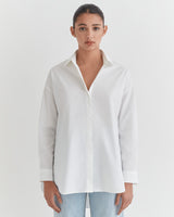 Woman in a button-down shirt and jeans standing against a plain background.