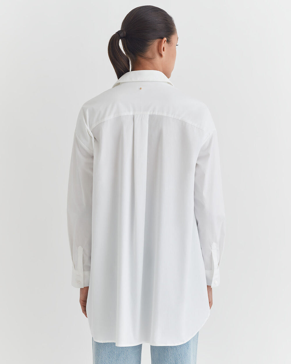 A person standing with their back to the camera, wearing a long-sleeved shirt and jeans.