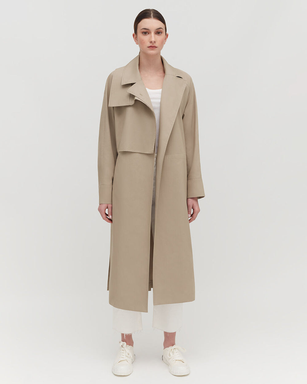 Woman standing in a coat with a collar and sneakers.