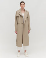 Woman standing in a coat with a collar and sneakers.