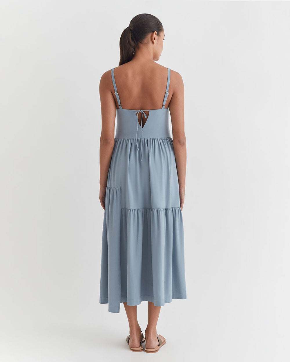 Woman seen from behind, wearing a mid-length dress, standing indoors.