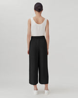Woman in a sleeveless top and cropped pants standing facing away.