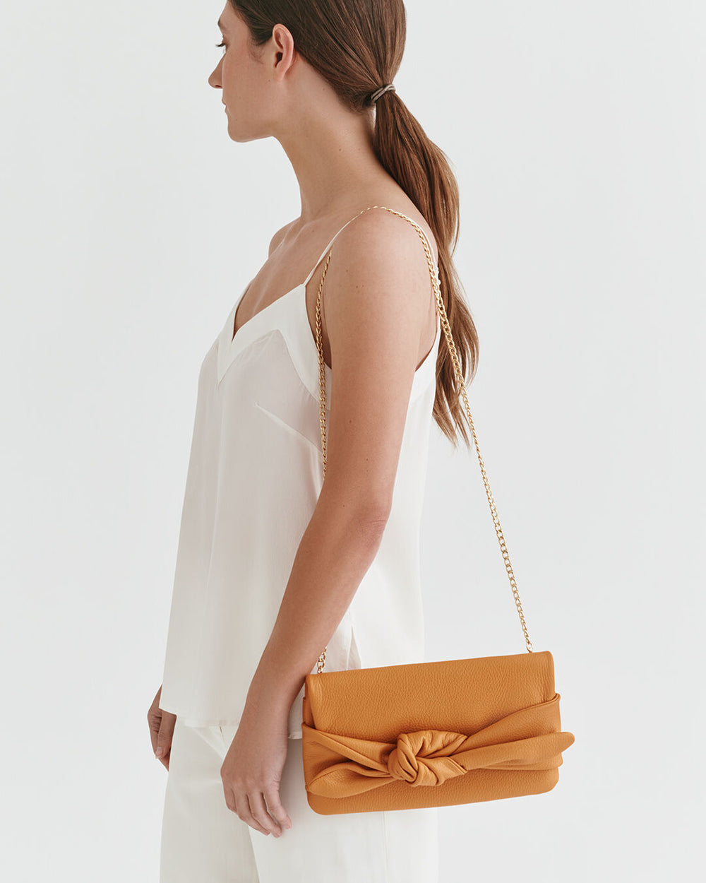 Woman holding a clutch with a chain, viewed from the side.