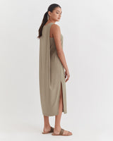 Woman in a sleeveless long dress standing sideways, looking over shoulder.