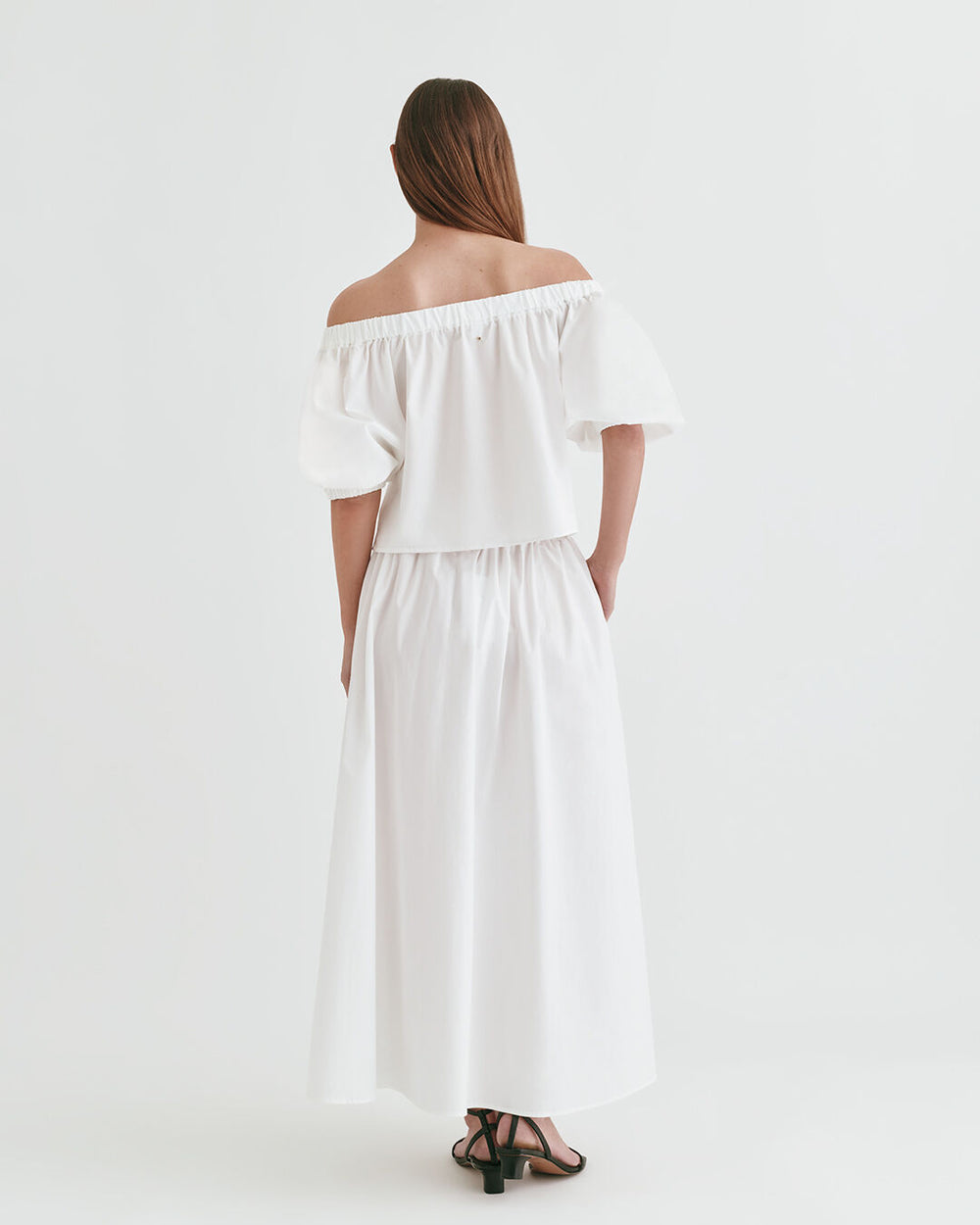 Woman wearing an off-shoulder dress, viewed from the back, standing against a plain background.