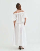 Woman wearing an off-shoulder dress, viewed from the back, standing against a plain background.