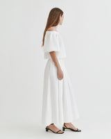 Woman standing sideways in a short-sleeved top and long skirt.