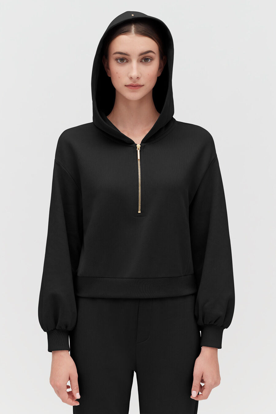 Woman in a hoodie standing with a neutral expression.