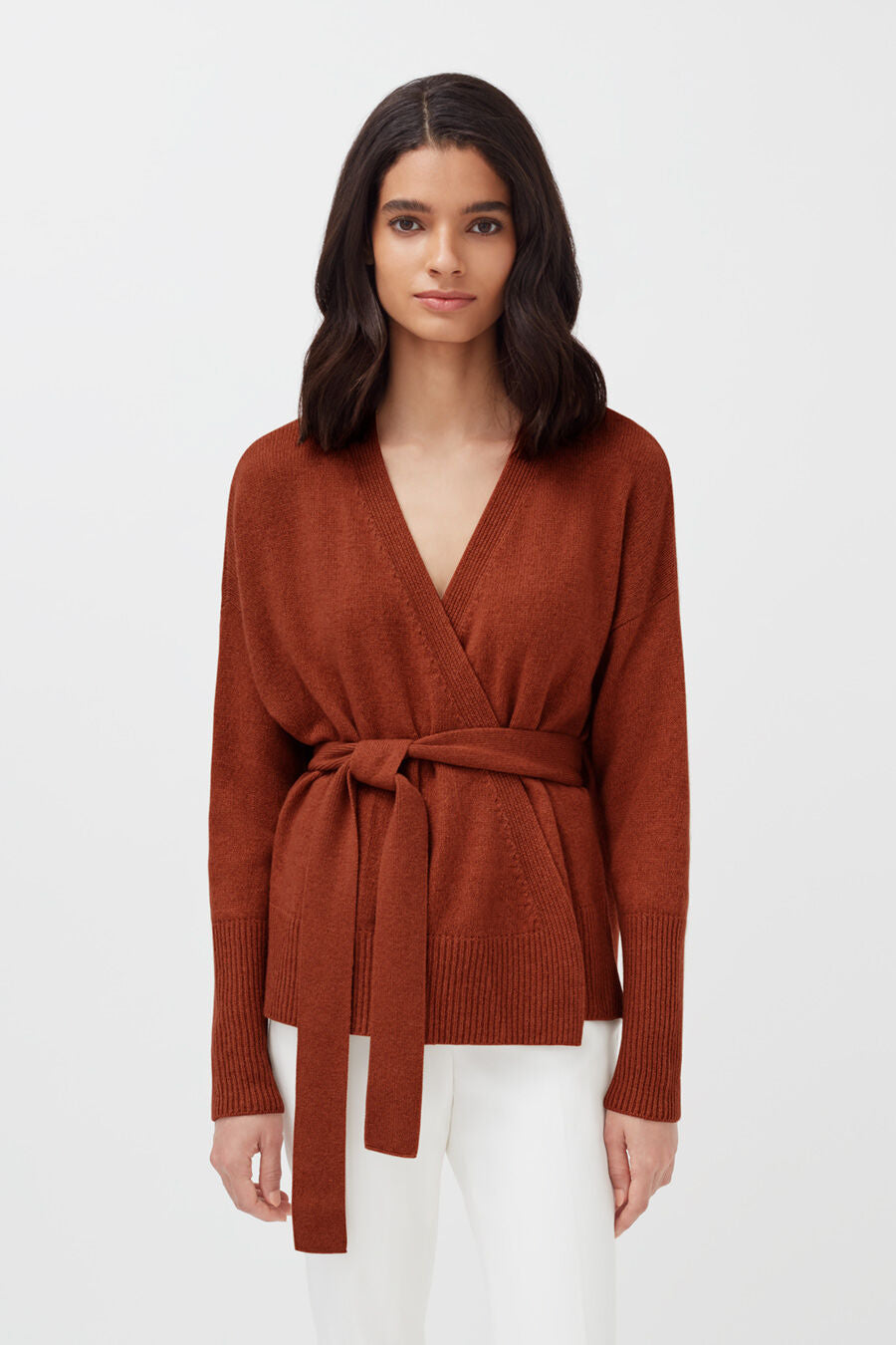 Woman in v-neck sweater with waist tie, standing.