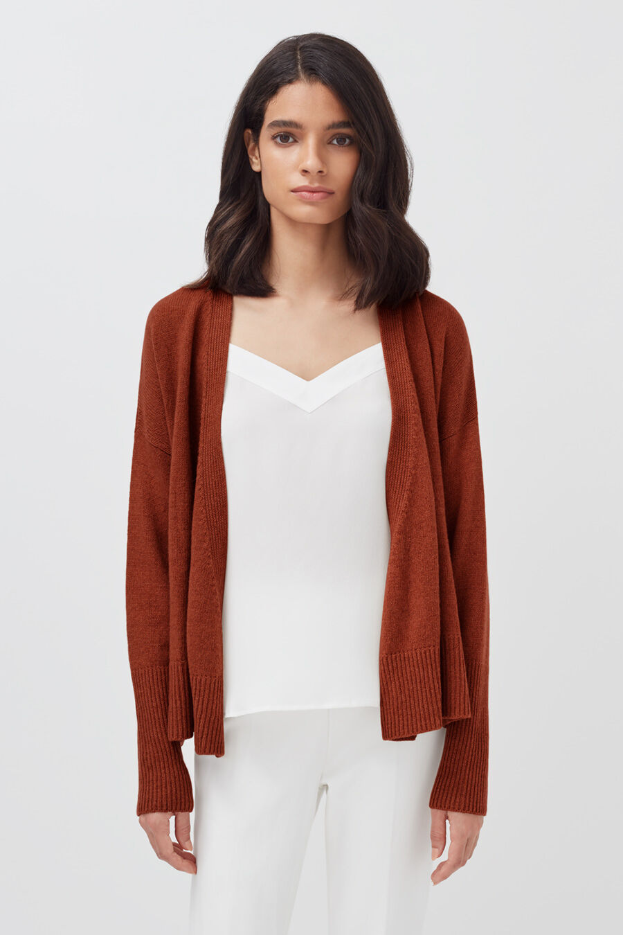 Woman standing in a cardigan and top, looking at the camera.