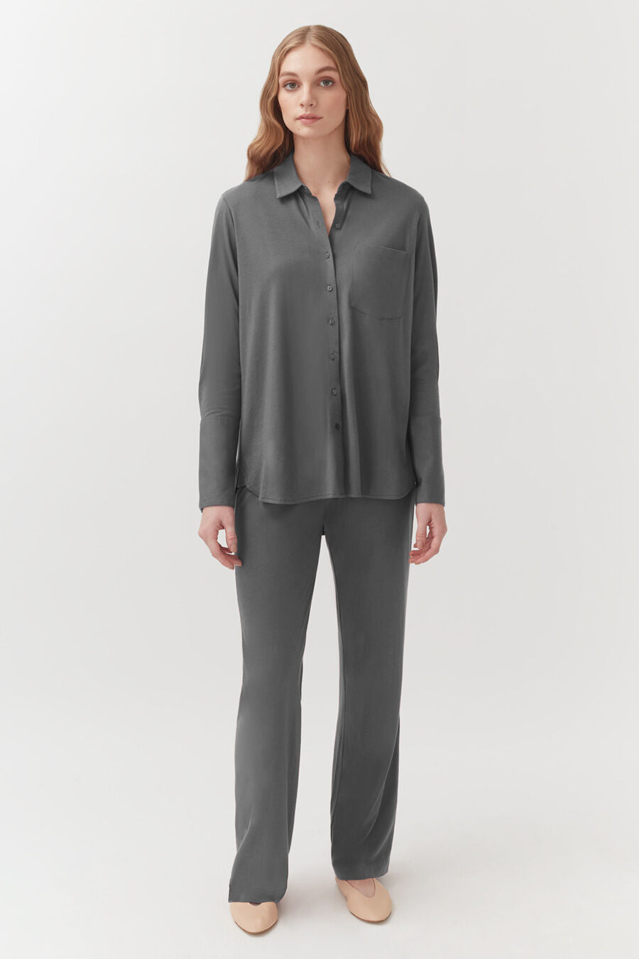 Woman standing in a buttoned shirt and pants with a neutral background.