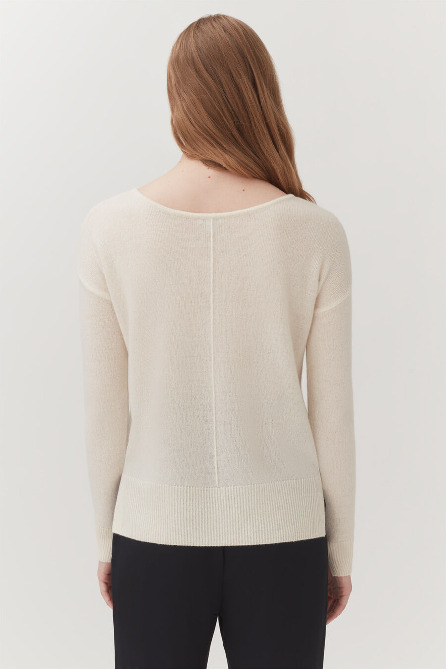 Rear view of a woman wearing a sweater and pants, standing.
