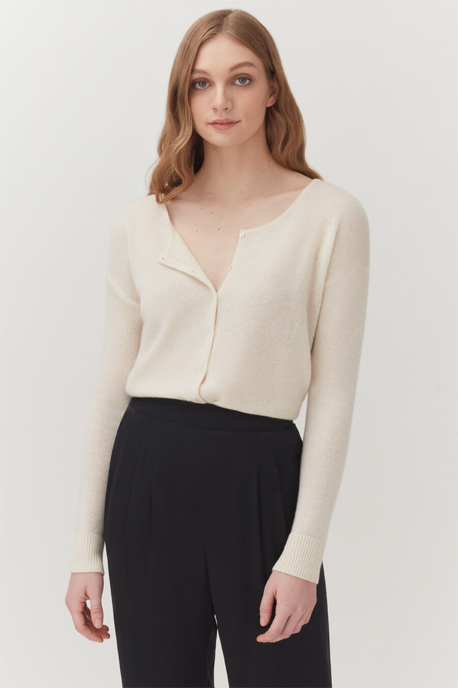 Woman wearing a buttoned sweater and trousers standing straight.