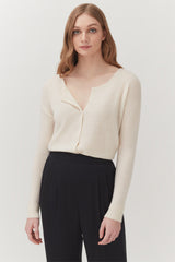 Woman wearing a buttoned sweater and trousers standing straight.