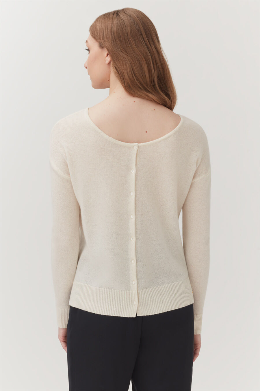 Woman wearing a cardigan with buttons on the back, standing.