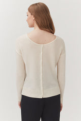 Woman wearing a cardigan with buttons on the back, standing.