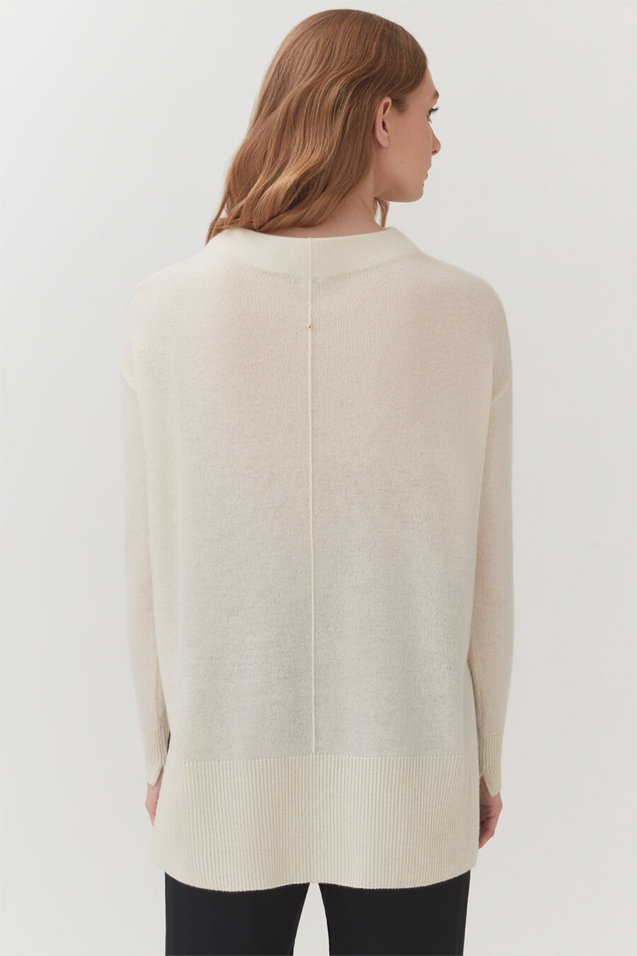 Woman standing, viewed from back, wearing a long-sleeved top and pants.